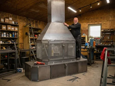 Simon Chénier à côté d'un foyer sur mesure géant dans l'atelier